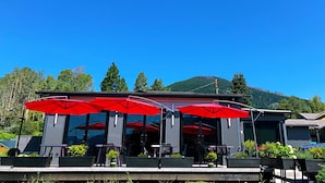 An outdoor seating area with red umbrellas, tables, and chairs, overlooking a mountainous landscape. - Kokanee Glacier Resort (Nelson)