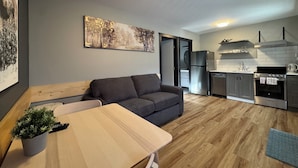 A modern apartment with a grey sofa, a wooden dining table, and a kitchen with stainless steel appliances. - Kokanee Glacier Resort (Nelson)