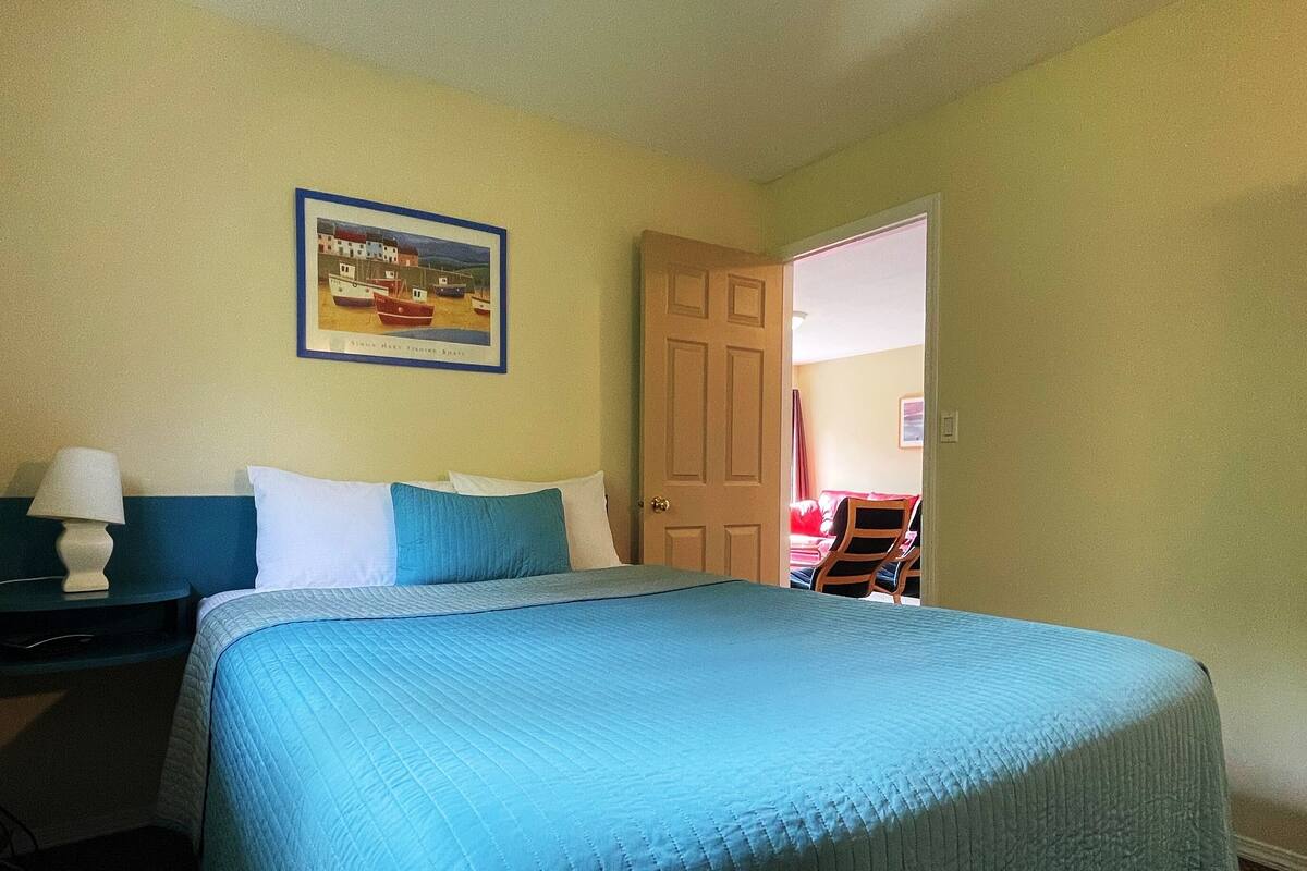 A hotel room with a bed, a nightstand, a lamp, and a door leading to another room.