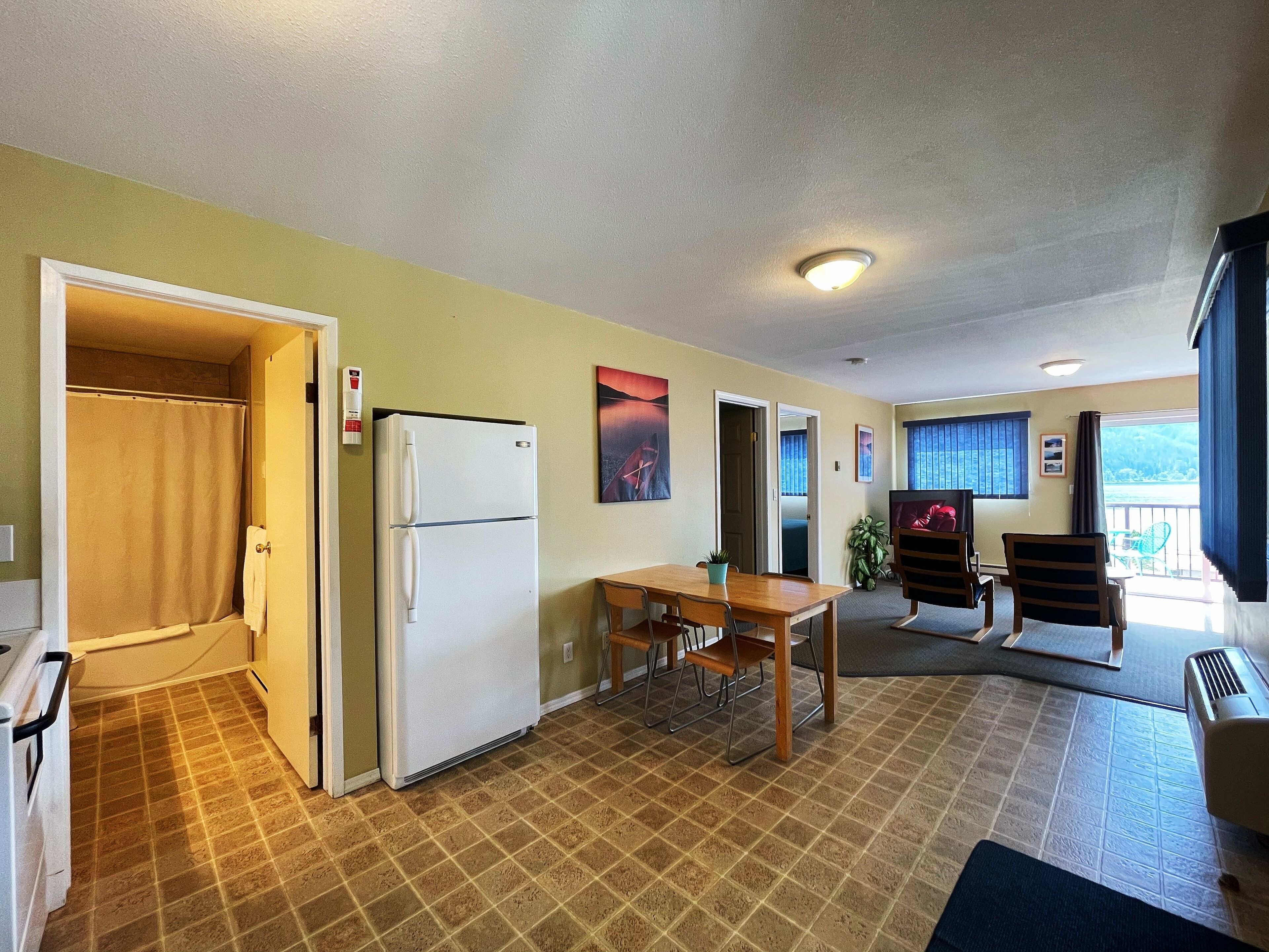 A compact hotel room with a kitchenette, a dining area, and a balcony with a view.