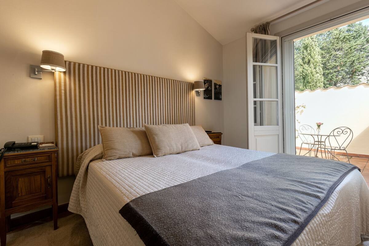 A bedroom with a bed, a bedside table, a lamp, and a view of the outdoors.