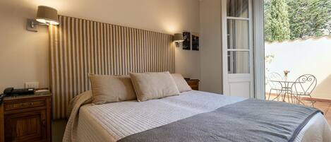 A bedroom with a bed, a bedside table, a lamp, and a view of the outdoors.