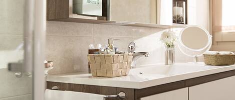 Une salle de bain avec un lavabo blanc, un miroir, un panier contenant des articles de toilette et un porte-serviettes.