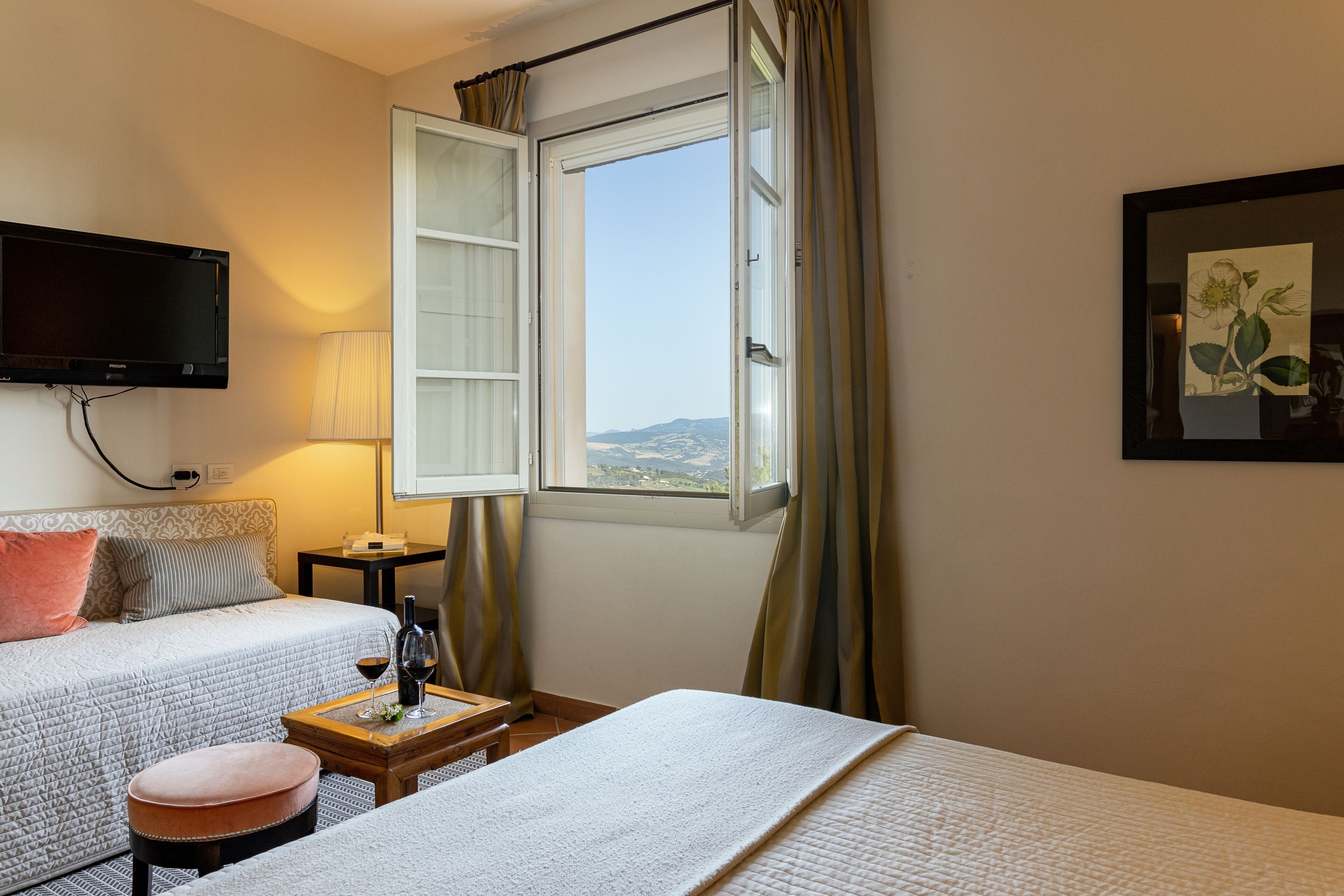 Habitación de hotel con dos camas, un televisor montado en la pared, una ventana con cortinas y vistas al paisaje.