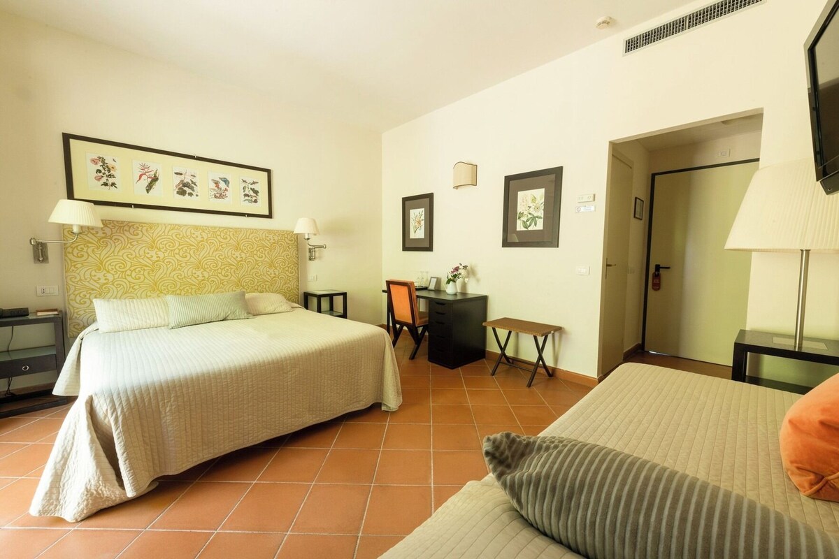 A hotel room with a bed, a desk, a chair, a small table, and a door.