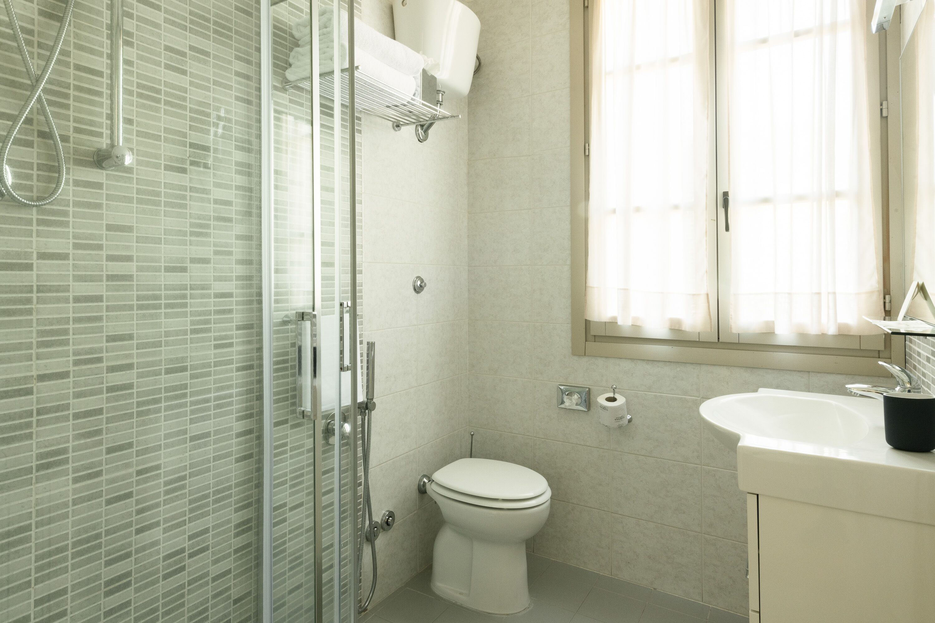 Un bany amb plat de dutxa de vidre, vàter i un lavabo amb mirall a sobre.
