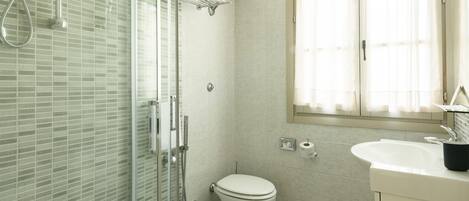 Un bagno con box doccia in vetro, un water e un lavandino con specchio sopra.