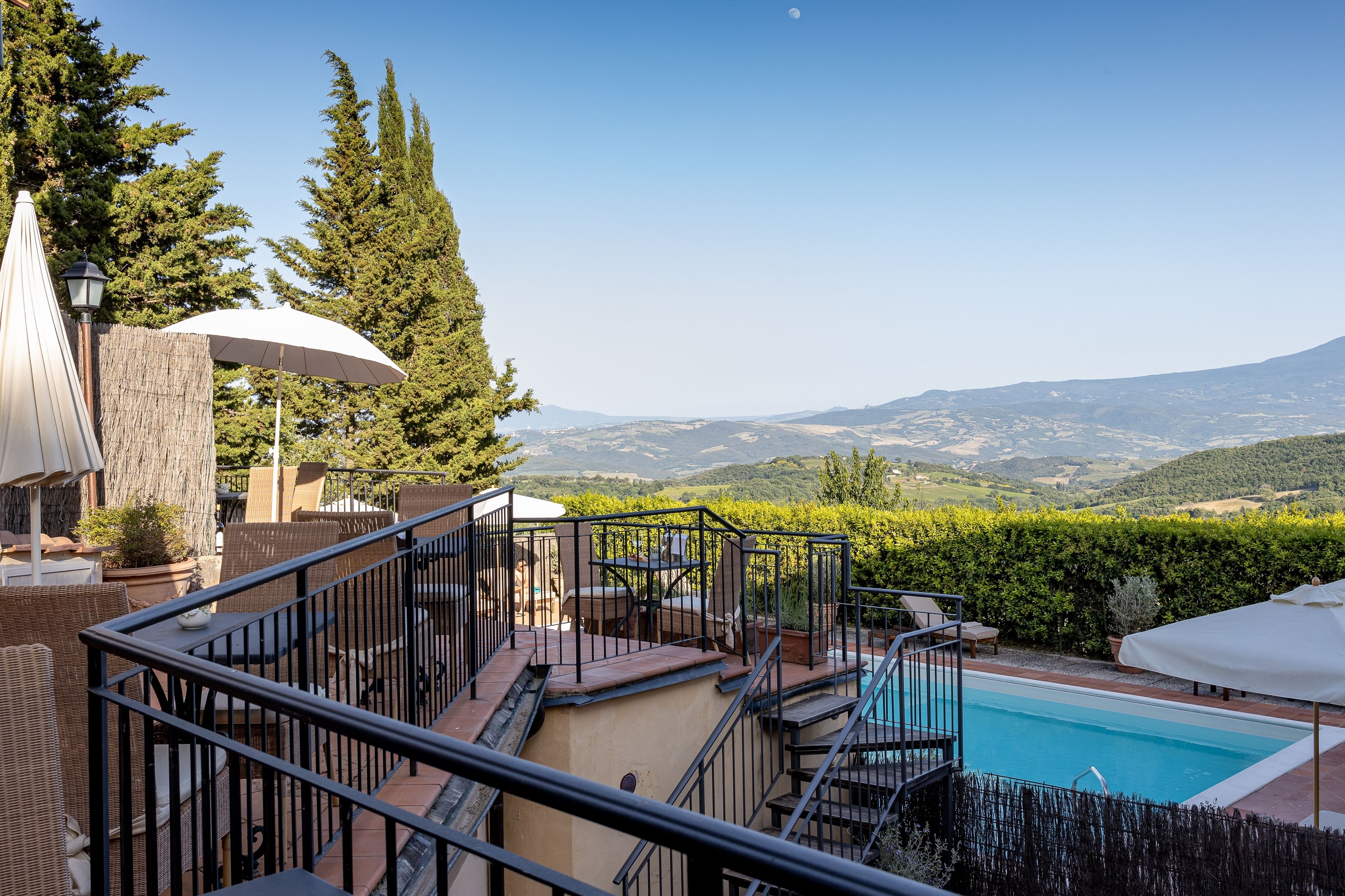 A pool area with a view of the mountains, outdoor furniture, and umbrellas.