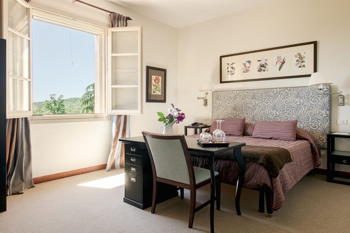 A bedroom with a bed, a desk, a chair, a dresser, and a window with a view of trees.