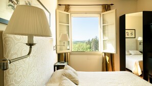 Habitación de hotel con una cama grande, una mesita de noche, una lámpara, una ventana con cortinas y vistas al exterior.