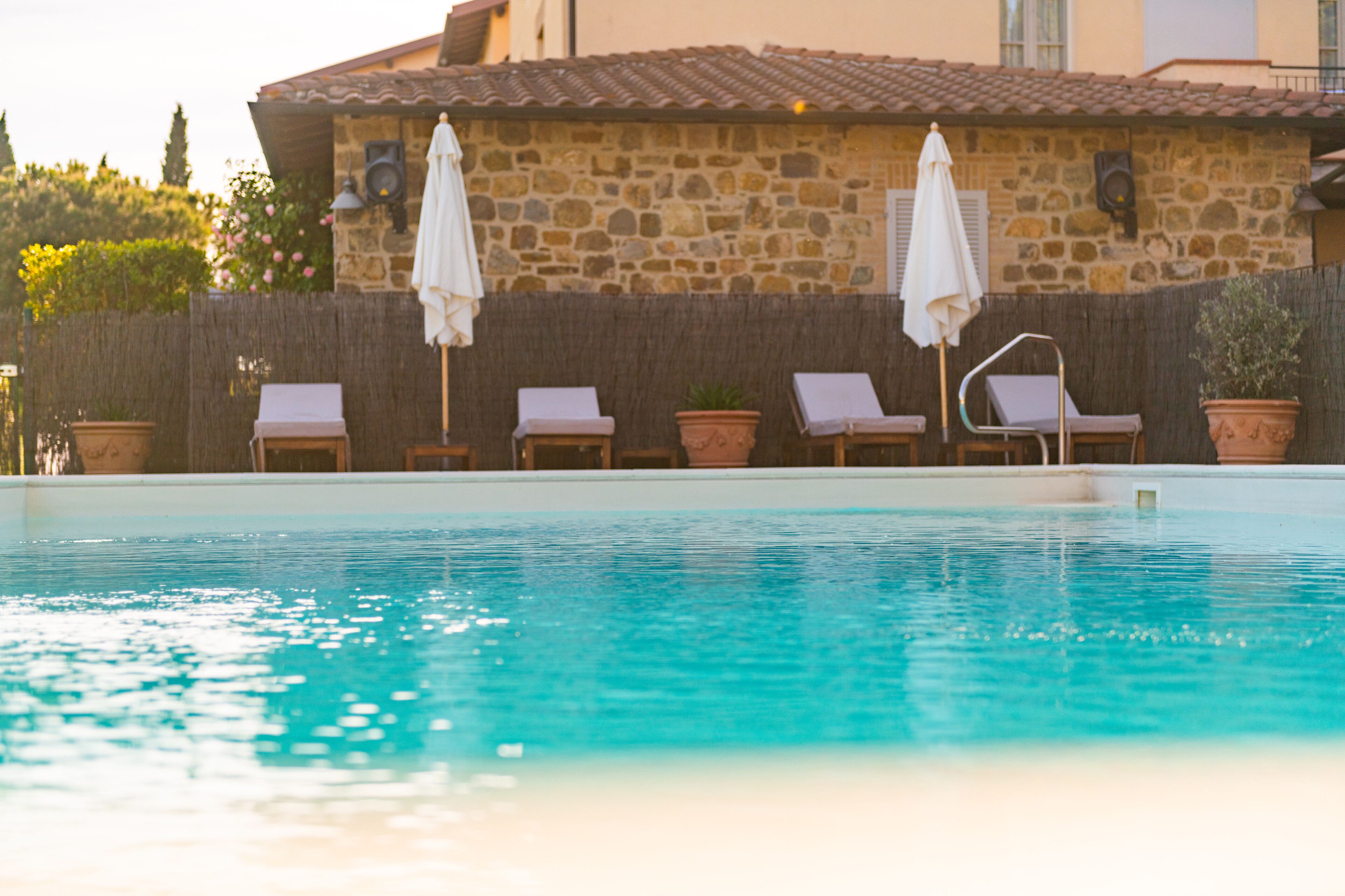 A swimming pool with lounge chairs and umbrellas, surrounded by a stone wall and potted plants.