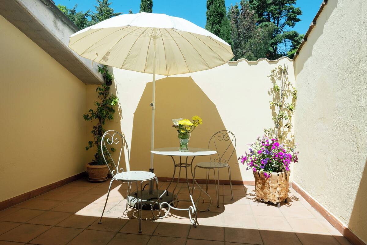 A patio with a table and chairs, a white umbrella, and potted plants.