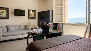 Una habitación de hotel con cama, sofá, mesa con un florero, televisión y ventana con vistas.