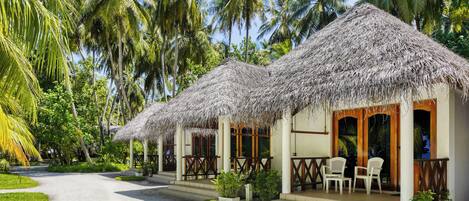 A resort with thatched-roof huts, a paved walkway, and lush greenery.