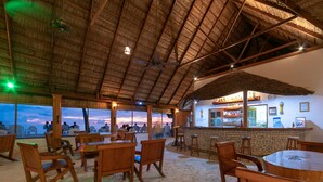 An indoor seating area with wooden furniture and a bar, overlooking a scenic sunset view. - Fihalhohi Maldives (Fihalhohi Island)
