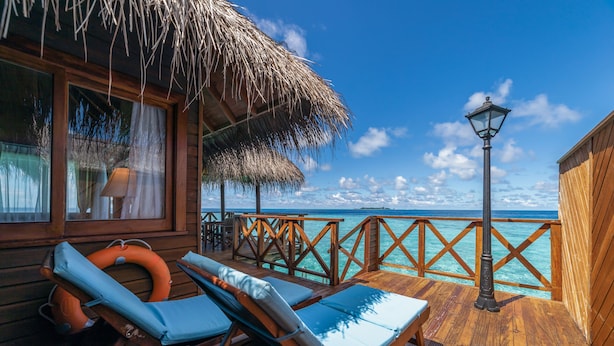 A wooden deck with two lounge chairs and a thatched roof structure. - Fihalhohi Maldives (Fihalhohi Island)