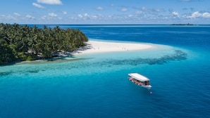 An aerial view of a tropical island with a white sandy beach, clear turquoise waters, and a boat docked near the shore. - Fihalhohi Maldives (Fihalhohi Island)