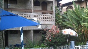 A two-story building with a balcony, a blue umbrella, and a stone wall with plants. - Canto do Mar (Ipojuca)