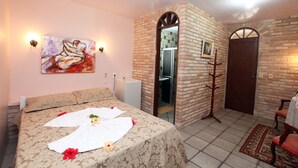 A hotel room with a bed, a painting, a brick wall, a door, and a coat rack. - Canto do Mar (Ipojuca)