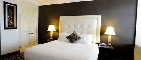 A hotel room with a large bed, two bedside tables with lamps, a door, and a framed picture on the wall.