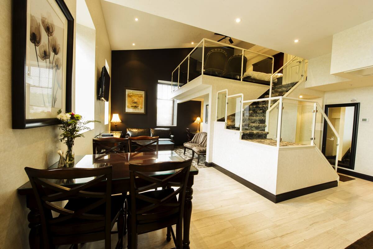 Un área de estar amplia con una mesa de comedor, sillas, un sofá y una escalera que conduce a un nivel superior.