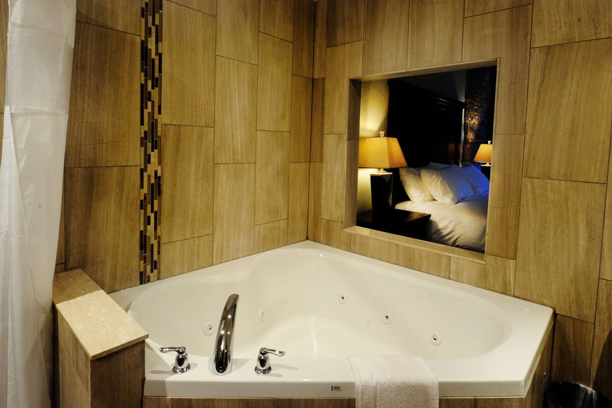 Un baño moderno con una bañera grande, un espejo y una mesita de noche con lámpara.