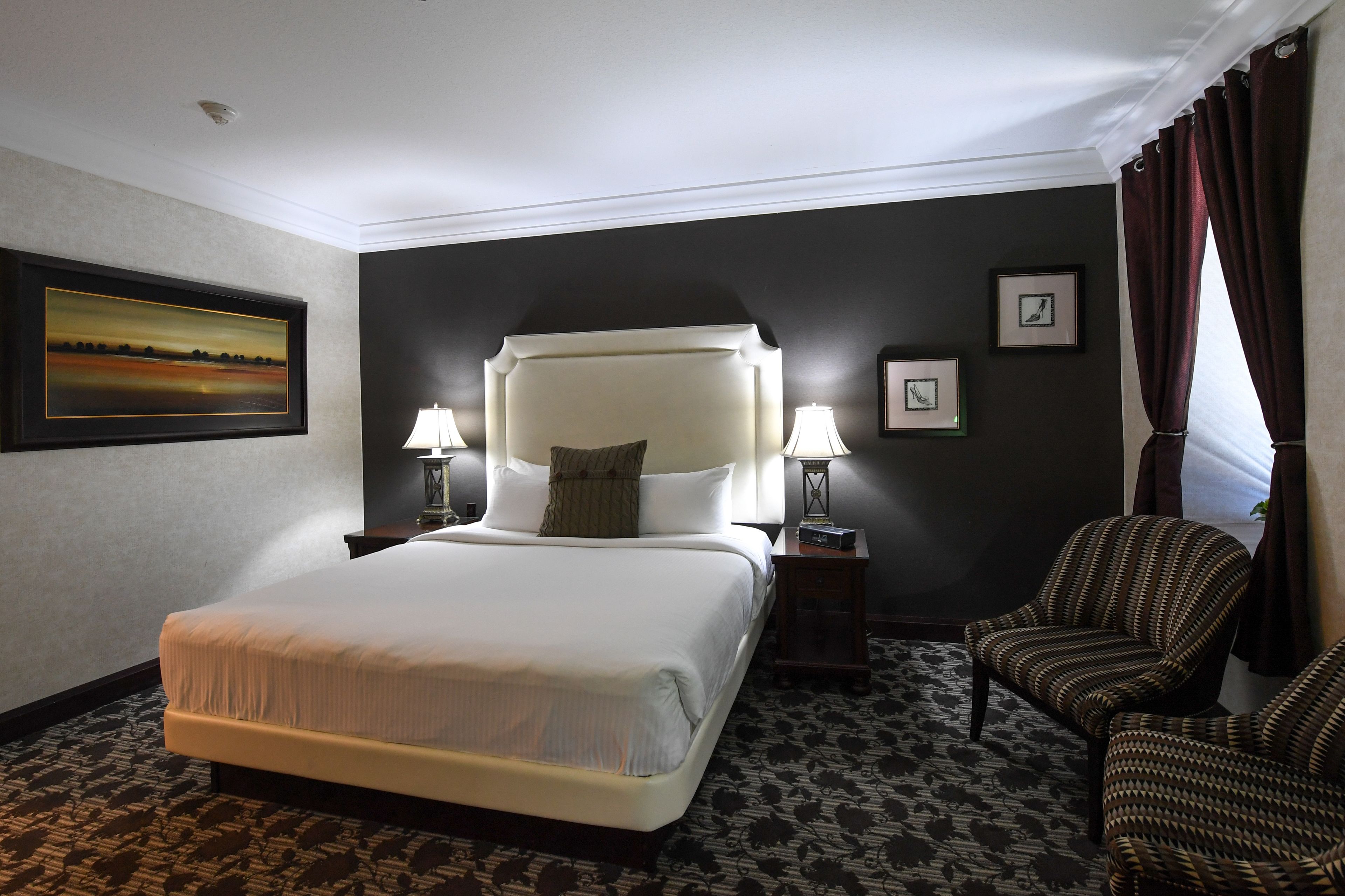 A hotel room with a large bed, two bedside tables with lamps, a chair, and a framed picture on the wall.