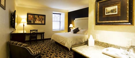 A hotel room with a bed, a desk, a chair, a television, and a framed picture on the wall.