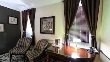 Habitación de hotel con dos sillones tapizados, una mesa de madera con una lámpara, un teléfono y obras de arte enmarcadas en las paredes.