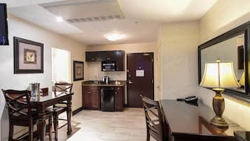 Habitación de hotel compacta con comedor, kitchenette y un espejo con lámpara.