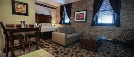 Habitación de hotel con una pared de acento de piedra, un comedor con una mesa y sillas de madera, un sofá, una mesa de centro y un ventilador de techo.