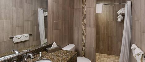 A modern bathroom with a granite countertop sink, a toilet, and a walk-in shower with a glass door.
