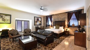 Quarto de hotel com cama, duas poltronas, um sofá, uma mesa de centro, uma escrivaninha e uma parede de destaque em pedra.