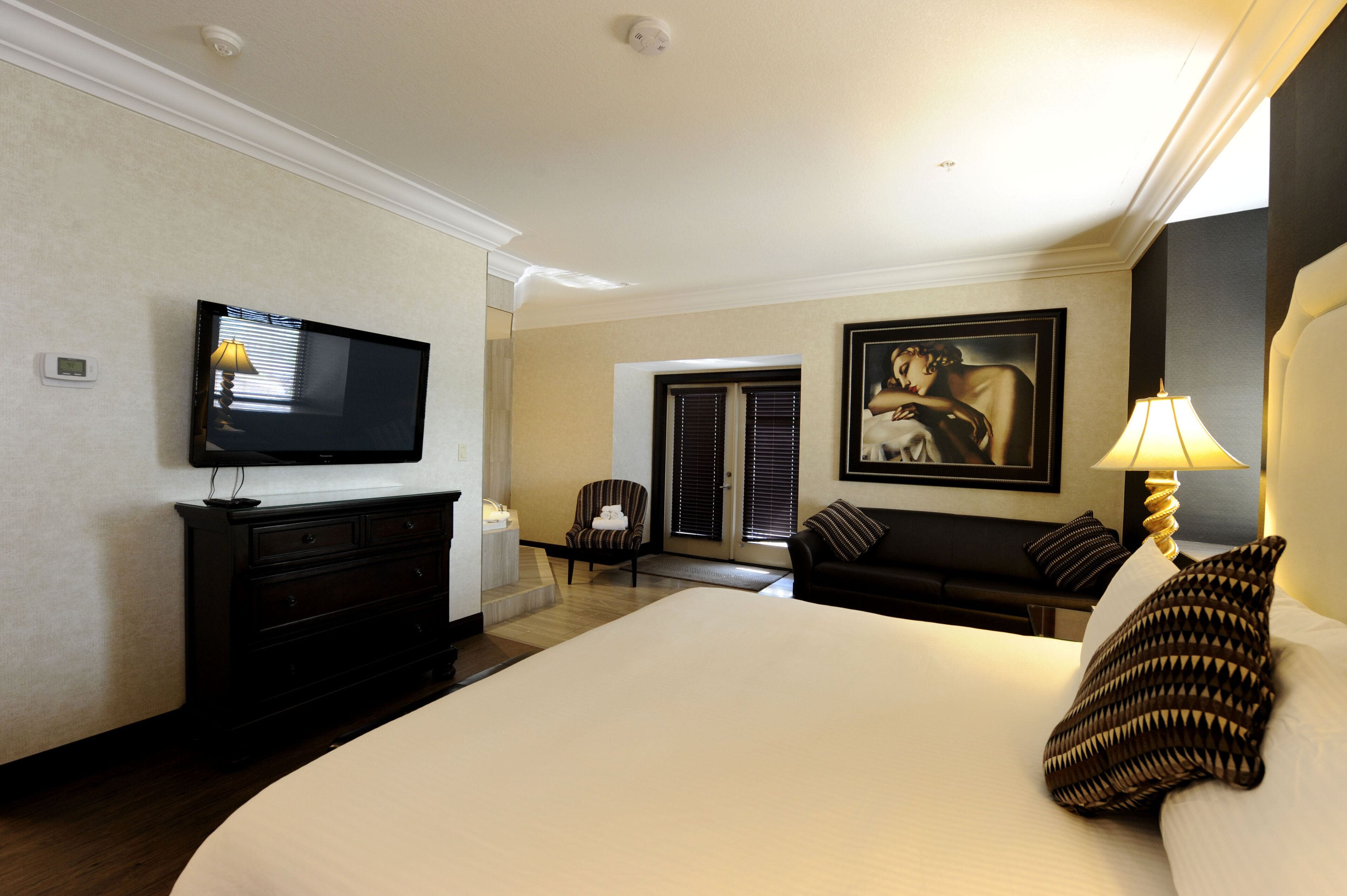 Una habitación de hotel con una cama grande, televisión, sofá, sillón y un cuadro en la pared.