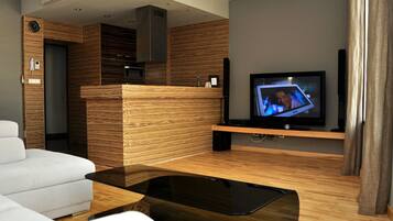 Una sala de estar moderna con un televisor de pantalla plana, un sofá blanco, una mesa de centro de madera y un escritorio de recepción integrado de madera.