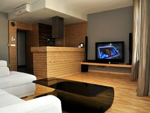 A modern living room with a flat-screen TV, a white sofa, a wooden coffee table, and a built-in wooden reception desk. - SleepWalker Boutique Suites (Wroclaw)
