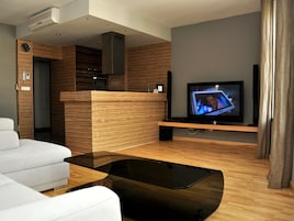 Una sala de estar moderna con un televisor de pantalla plana, un sofá blanco, una mesa de centro de madera y un escritorio de recepción integrado de madera.