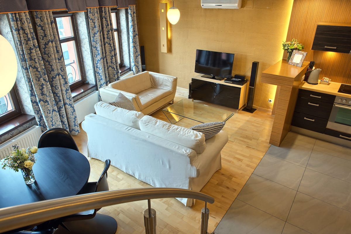 A modern living room with a sofa, TV, and a small kitchen area with a stove and cabinets.