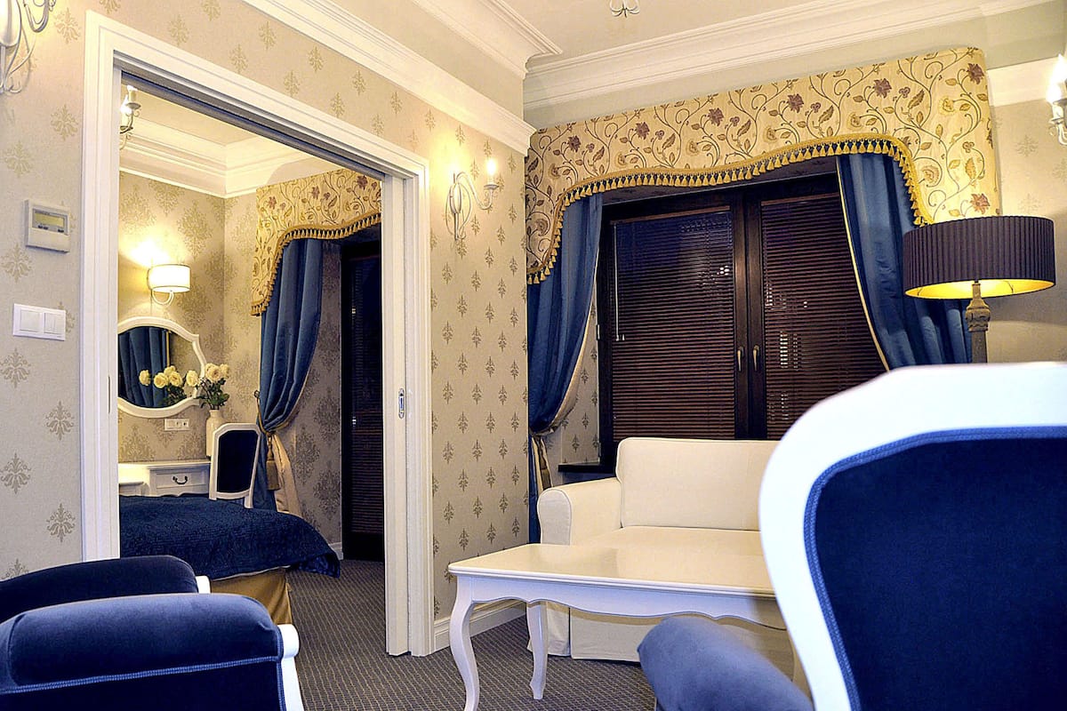 A hotel room with a sitting area, a small table, a mirror, and a wardrobe.