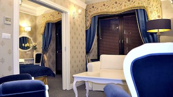 A hotel room with a sitting area, a small table, a mirror, and a wardrobe.