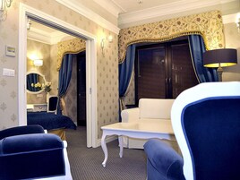 A hotel room with a sitting area, a small table, a mirror, and a wardrobe.