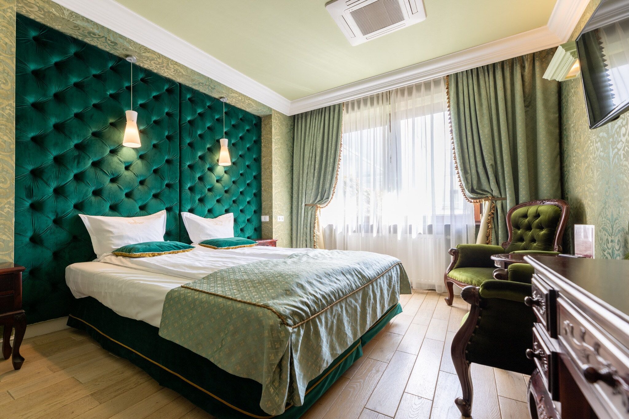Un dormitorio con una cama grande, cabecera tapizada de color verde y cómoda de madera clásica.