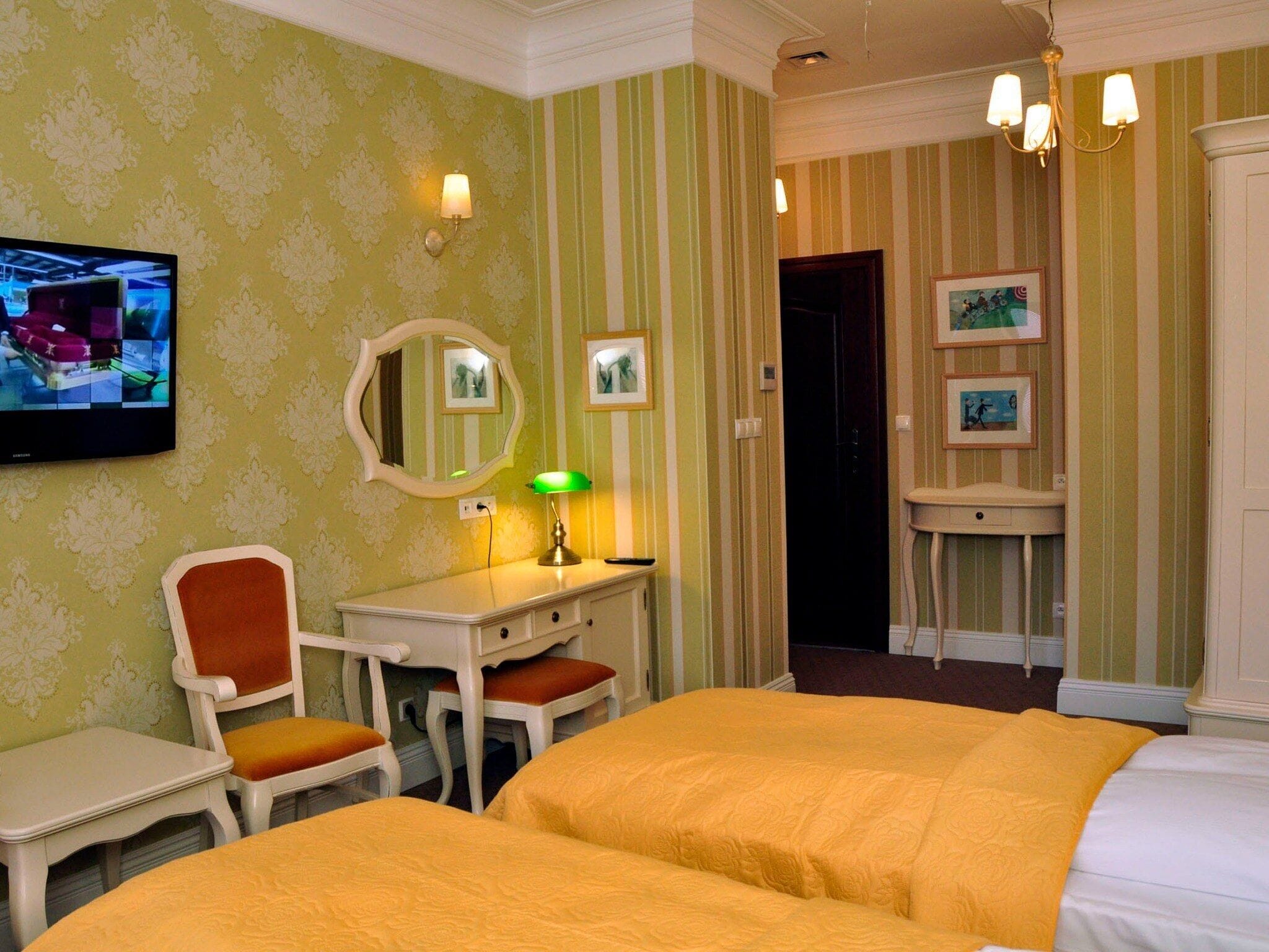 Ein Hotelzimmer mit zwei Betten, einem Schreibtisch mit Stuhl, einem Fernseher und einem Spiegel.