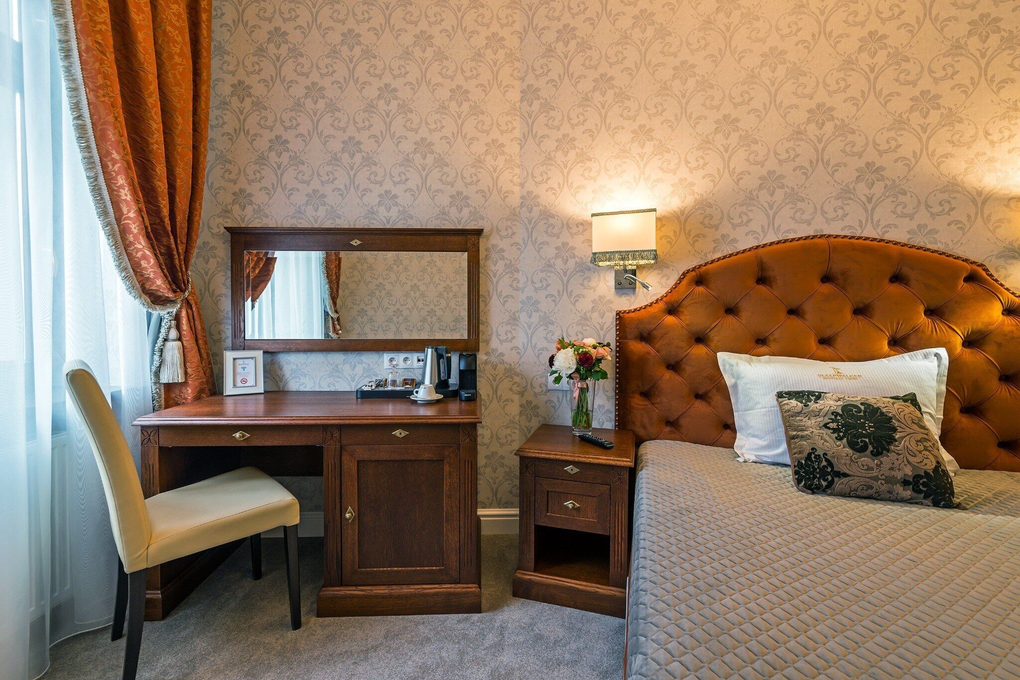 Een hotelkamer met een houten bureau, een stoel, een bed met een gestuufd hoofdeinde en een nachtkastje.