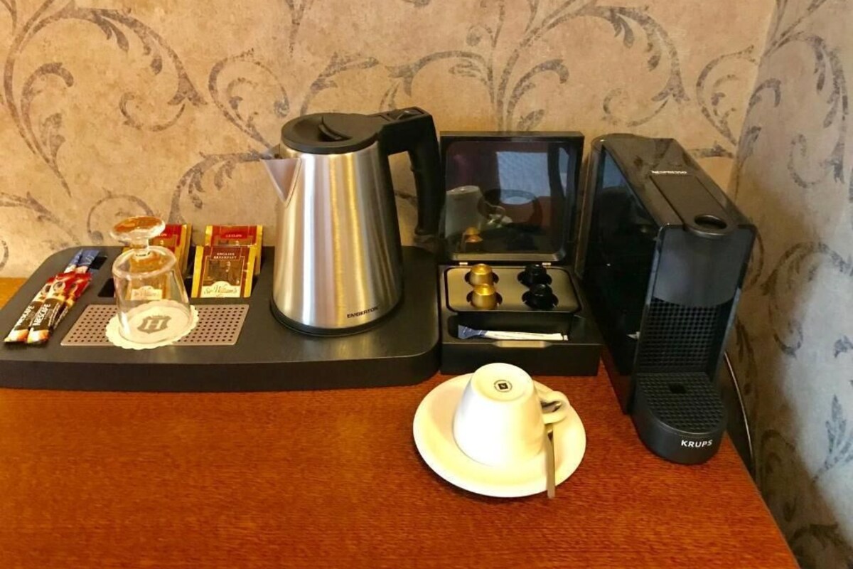 A coffee station with a coffee maker, a kettle, a cup, and some snacks on a tray.