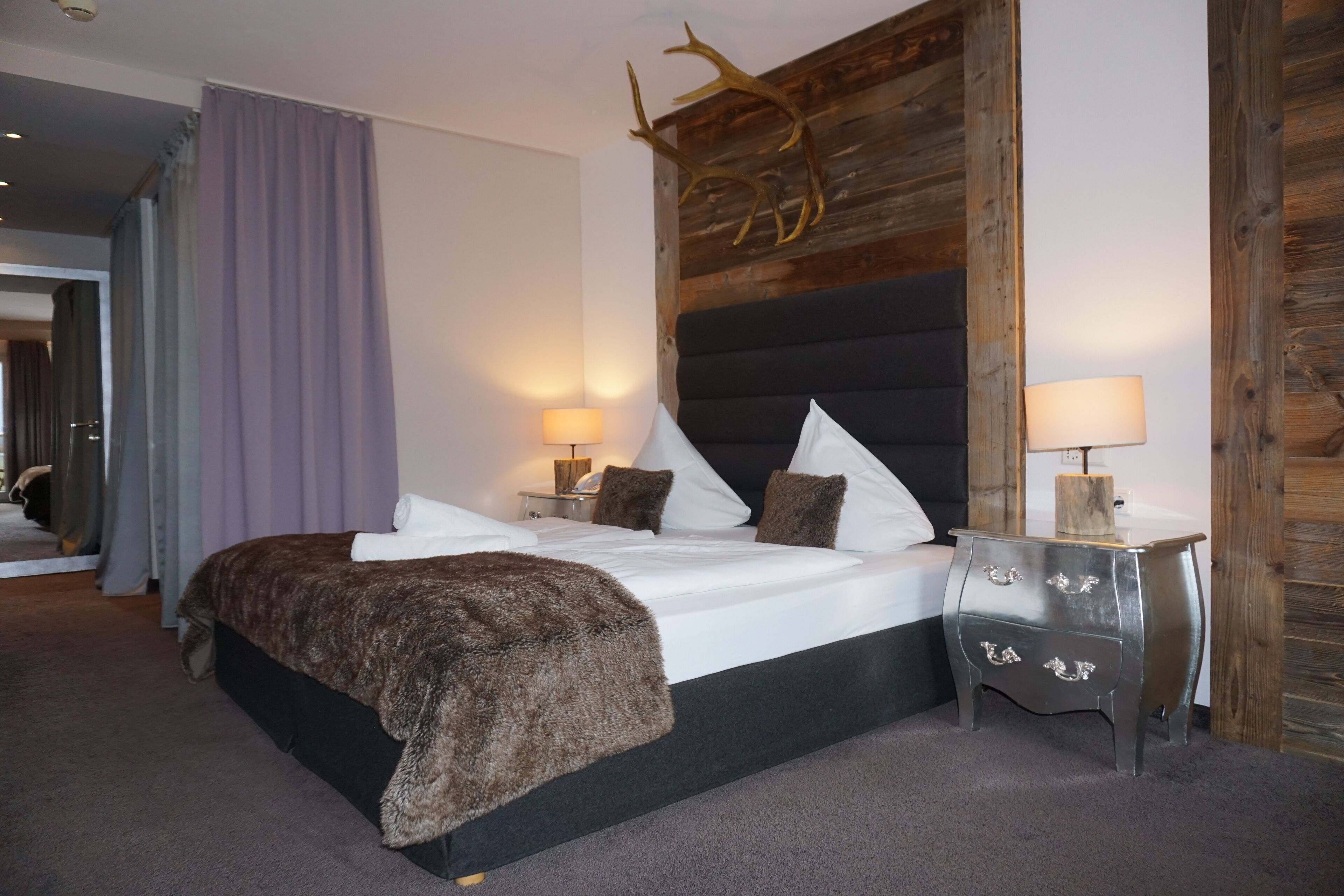 Une chambre à coucher avec un grand lit, deux tables de chevet avec des lampes, une tête de lit en bois et un miroir.