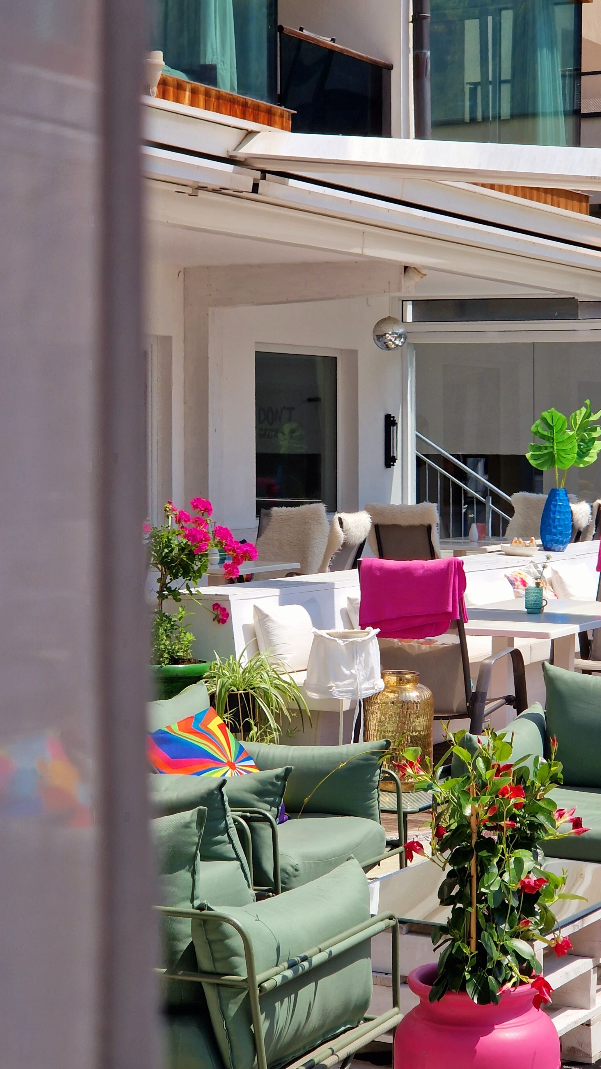 An outdoor seating area with green cushioned chairs, a table with a pink towel, and various potted plants.