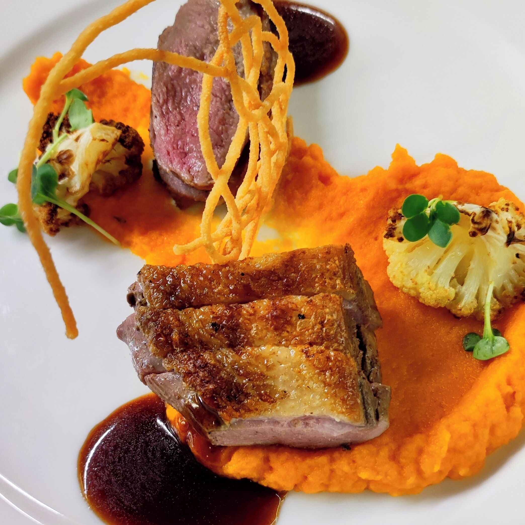 A plate of food with a piece of meat, vegetables, and a sauce.