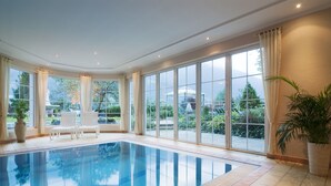 Una amplia piscina interior con paredes de vidrio transparente, sillas blancas y una planta en maceta.