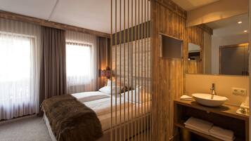 Een moderne hotelkamer met een bed, een houten scheidingswand, een badkamer met wastafel en spiegel, en een raam met gordijnen.